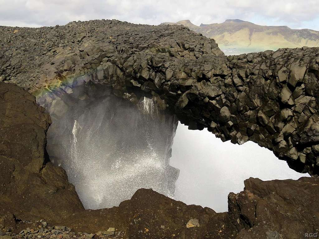 A rainbow is left in the aftermath of a wave crashing through a blowhole at Dyrhólaey