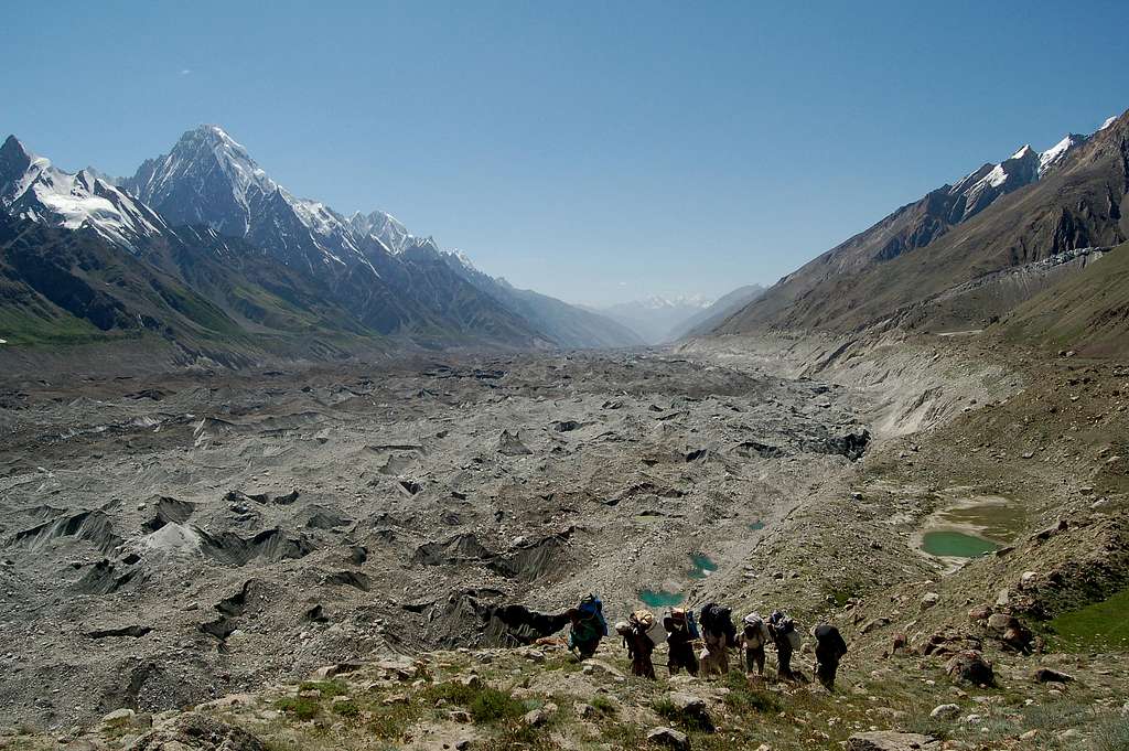 Porters trekking through the many meadows between the Pumari Chhish and Jutmo Glaciers with Makrong Chhish rising in the background