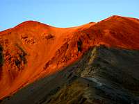 Morning Alpenglow burns on Redcloud Peak as a lone hiker heads up