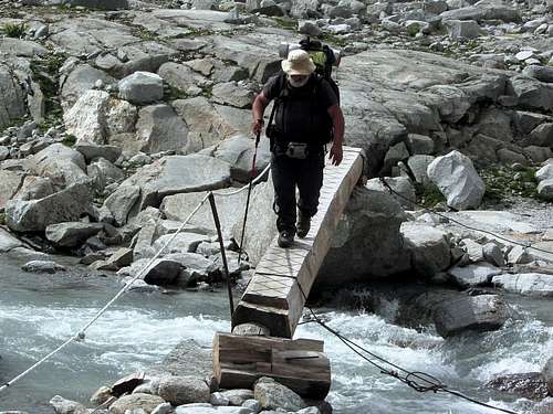 A heavily loaded long distance hiker crossing a stream on the Neveser Höhenweg